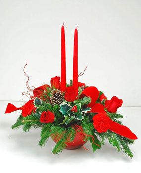 Glowing twin candles are the center of attention in this arrangement.  A red glass vase with silver star design is filled with red roses, red carnations