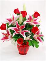 Clear red glass vase arrangement filled with red roses white baby breath and highlighted with stargazer lilies and mixed greenery. This arrangement is sure to send the message you wish to convey