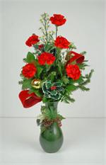 Christmas Joy is a arrangement of six holiday red carnations, holiday greens, holly, red velvet ribbons, sun spring asters and gold oraments, all arranged in a Christmas green ceramic vase with holiday trim. Share the joy of the season with your family an