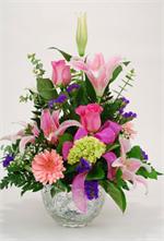 Pink lilies with pink roses, green hydrangeas, pink gerbera, and purple statice, mixed greens and million star baby breath are designed in a crystal handle keepsake basket.