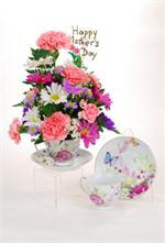 Make a lasting impression this Mother's Day with a thoughtful cup and saucer floral arrangement. Pink carnations with lavender and white daisys and mixed greens are designed in a tea cup and saucer with a rose and  butterfly motif.  Tell Mom how much she 