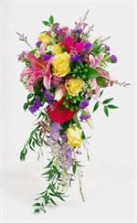Yellow roses with red gerberas, starfighter lilies, purple statice, lavender larkspur with white wax flower and Italian ruscus