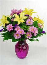 The name says it all, “Harmony”. This richly colored purple glass vase is filled with bright yellow Asiatic lilies, lavender spray daisies, with yellow solid ago, purple statice, and mixed greens. Call today, and your gift of kindness will be on it’s way