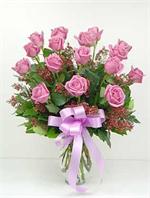 12 Lavender Roses arranged in a glass vase with mixed greenery and wax flower