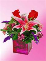 Hand designed in a colorful glass cube vase are red roses with pink stargazer lilies, pink carnations with wax flower, and purple static. Arranged, hand delivered and ready to enjoy. Need it today? Just call by 2 P.M and your gift will arrive the same day